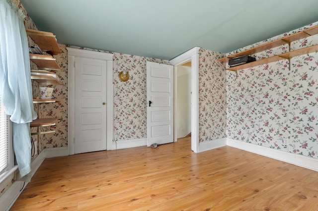 spare room with wallpapered walls, light wood-style flooring, and baseboards