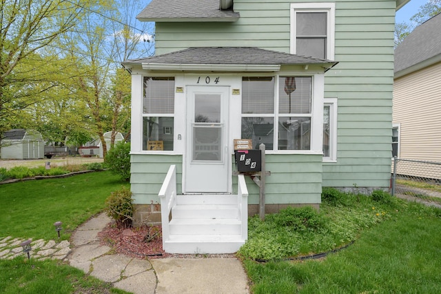 doorway to property featuring a yard, roof with shingles, and fence