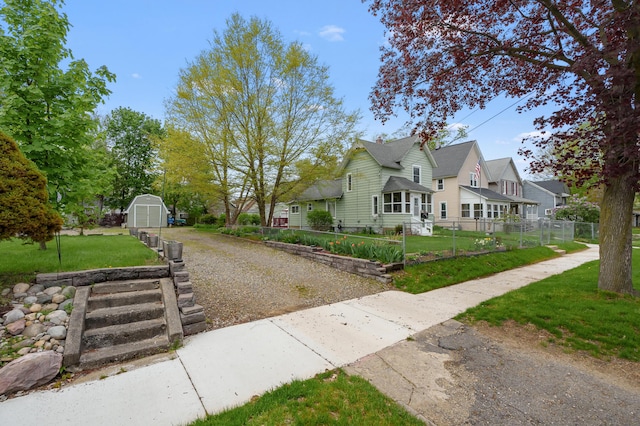 bungalow-style home with fence, a storage shed, an outdoor structure, driveway, and a front lawn