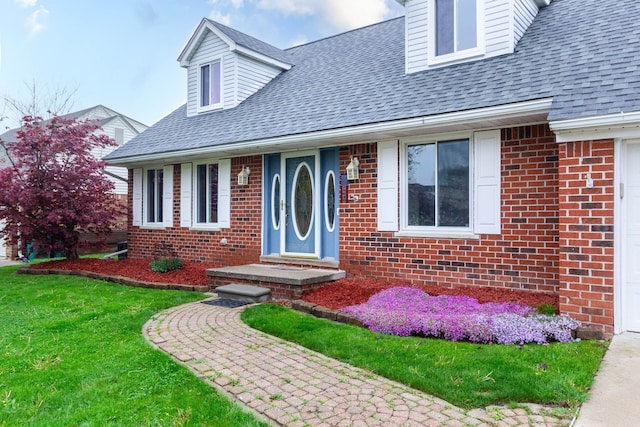 cape cod house with a shingled roof, brick siding, and a front yard
