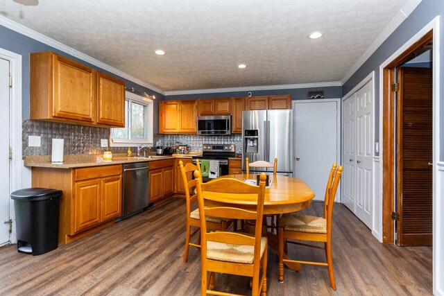 kitchen featuring dark wood finished floors, a sink, crown molding, decorative backsplash, and stainless steel appliances