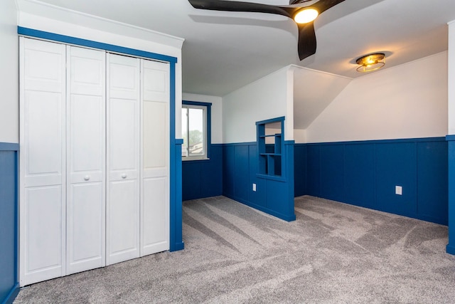unfurnished bedroom featuring lofted ceiling, a closet, a wainscoted wall, ceiling fan, and carpet flooring