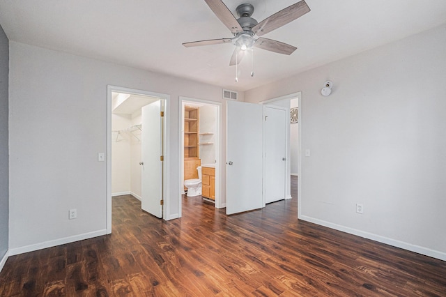 unfurnished bedroom with baseboards, dark wood-style flooring, visible vents, and a walk in closet