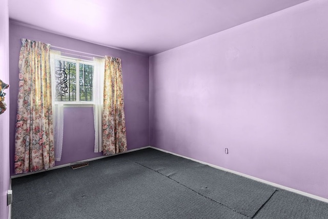 empty room featuring dark colored carpet and baseboards