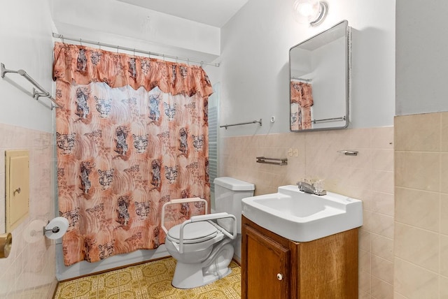 bathroom featuring tile walls, toilet, vanity, shower / bath combination with curtain, and a wainscoted wall