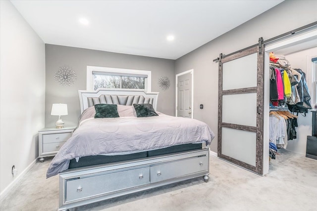bedroom with a closet, a barn door, baseboards, a spacious closet, and light colored carpet