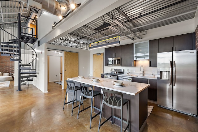 kitchen with appliances with stainless steel finishes, concrete flooring, a kitchen bar, and a sink