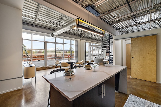 kitchen with a towering ceiling, light stone counters, baseboards, a kitchen island, and concrete floors