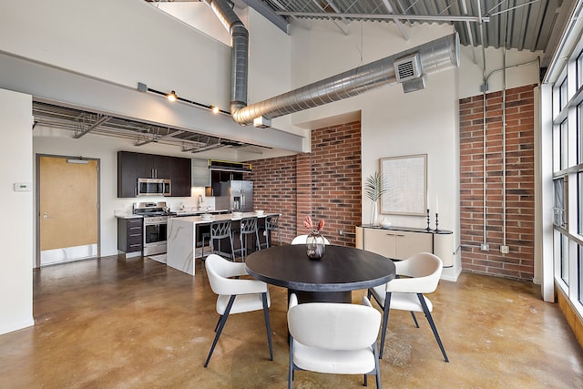 dining area featuring baseboards, brick wall, concrete flooring, and a towering ceiling