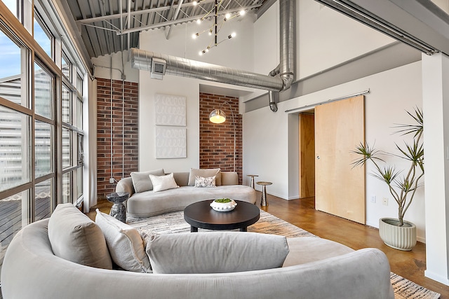 living area featuring wood finished floors, a towering ceiling, visible vents, brick wall, and baseboards