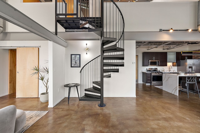 staircase featuring a towering ceiling, concrete flooring, and baseboards