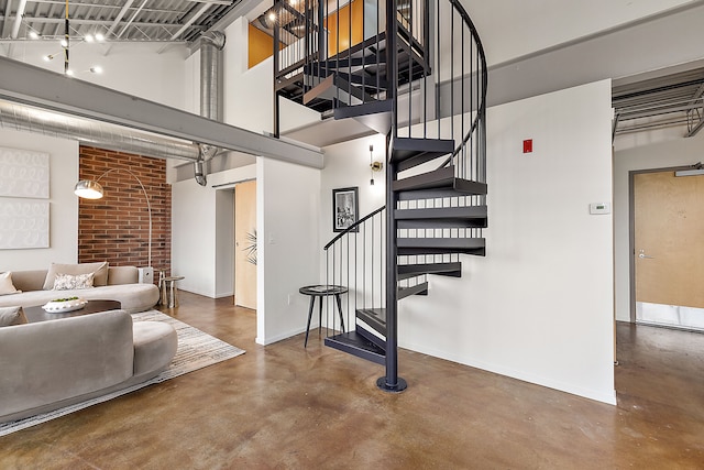 stairway with baseboards, concrete floors, and a towering ceiling