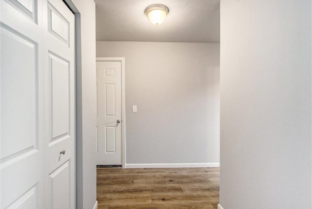 hall featuring baseboards, a textured ceiling, and wood finished floors
