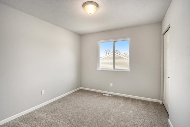 spare room featuring carpet flooring, a textured ceiling, visible vents, and baseboards