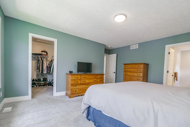 carpeted bedroom featuring a closet, visible vents, baseboards, and a walk in closet