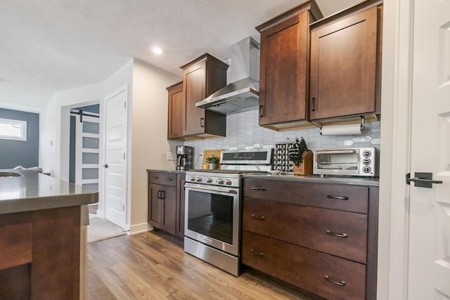 kitchen featuring wall chimney range hood, a toaster, stainless steel range with gas stovetop, and dark countertops