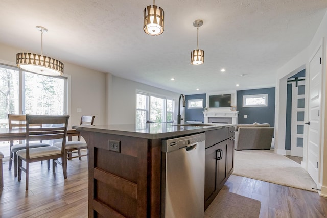 kitchen with a sink, a kitchen island with sink, a healthy amount of sunlight, dishwasher, and dark countertops