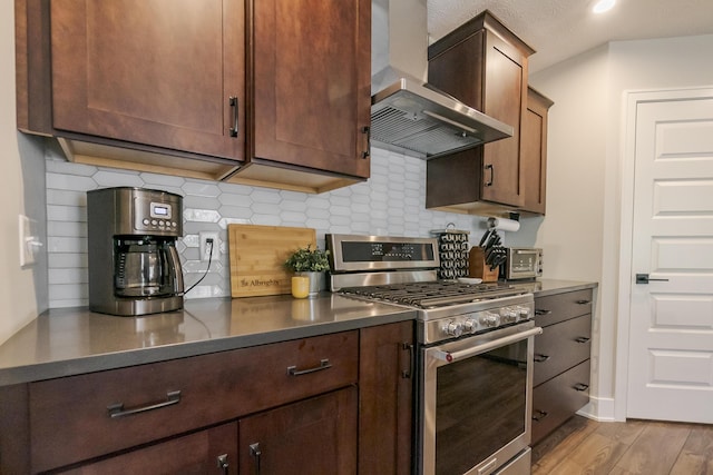 kitchen featuring wall chimney exhaust hood, decorative backsplash, wood finished floors, and stainless steel gas stove
