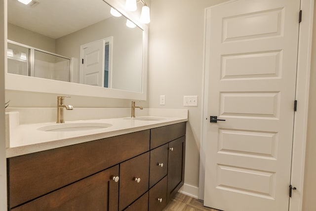 full bathroom with a stall shower, baseboards, double vanity, and a sink