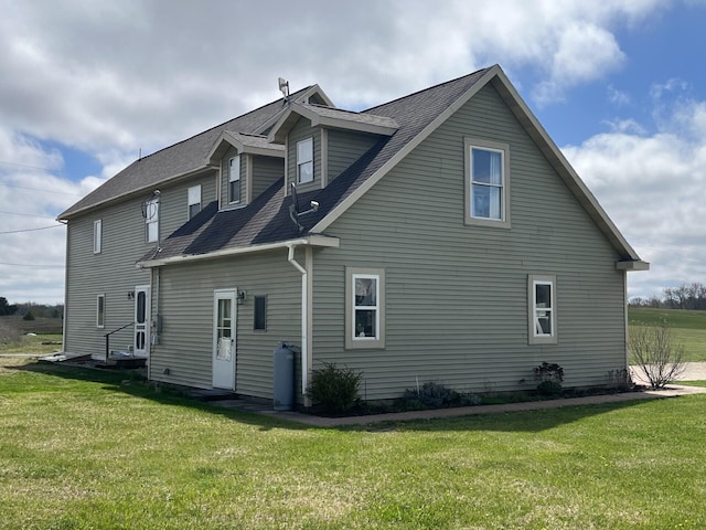 rear view of property featuring a shingled roof, a yard, and entry steps