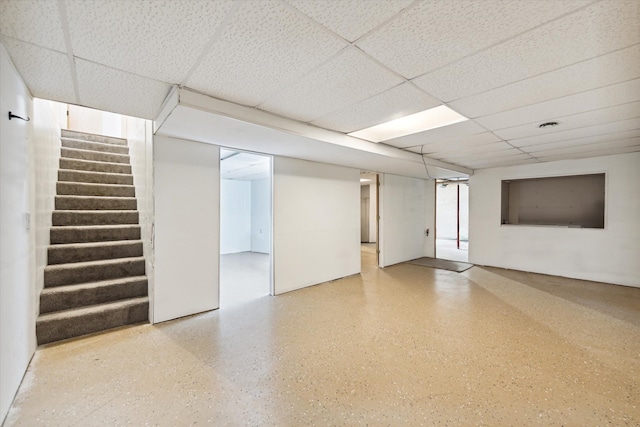 finished below grade area featuring a paneled ceiling and stairway