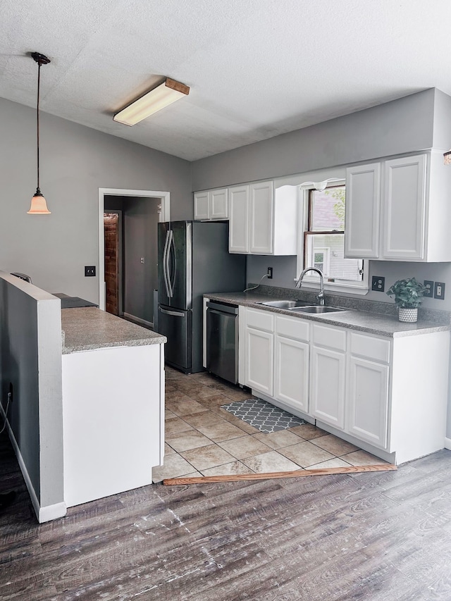 kitchen with a sink, light wood-style flooring, white cabinetry, hanging light fixtures, and appliances with stainless steel finishes