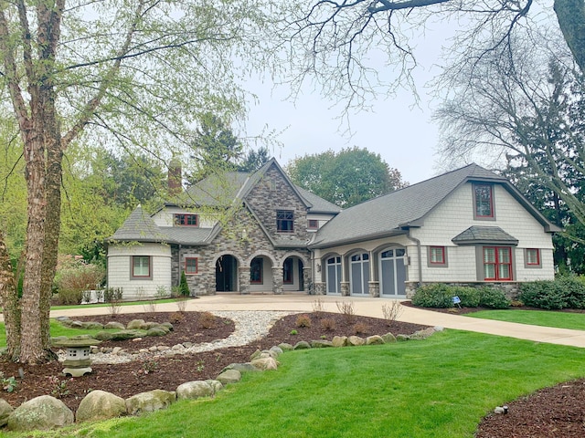 french country style house with stone siding, curved driveway, a front yard, and a chimney