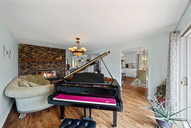 living area featuring baseboards, a brick fireplace, a chandelier, and wood finished floors