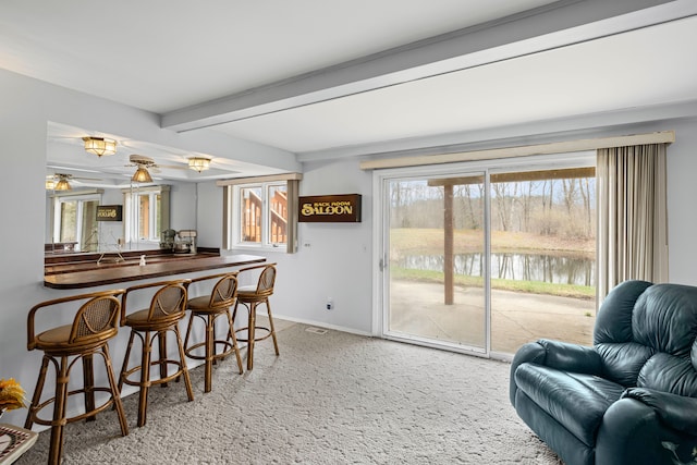 carpeted dining area featuring baseboards, beamed ceiling, a water view, and ceiling fan