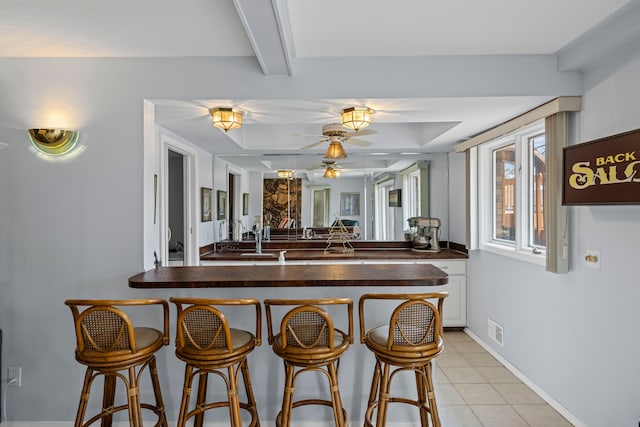 kitchen with a peninsula, a breakfast bar area, visible vents, beamed ceiling, and light tile patterned floors