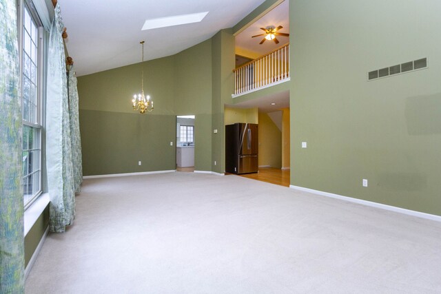 carpeted empty room featuring a skylight, high vaulted ceiling, a chandelier, baseboards, and a ceiling fan