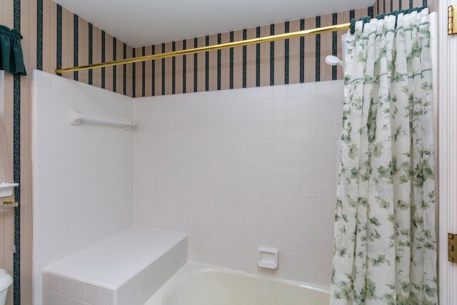 bathroom with wallpapered walls and shower / tub combo