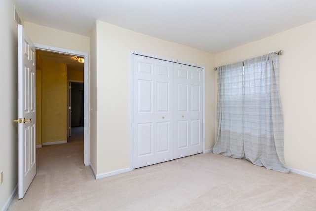 unfurnished bedroom with light colored carpet, a closet, and baseboards