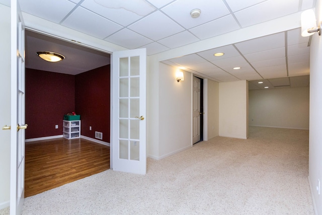 basement featuring french doors, carpet flooring, baseboards, and a drop ceiling