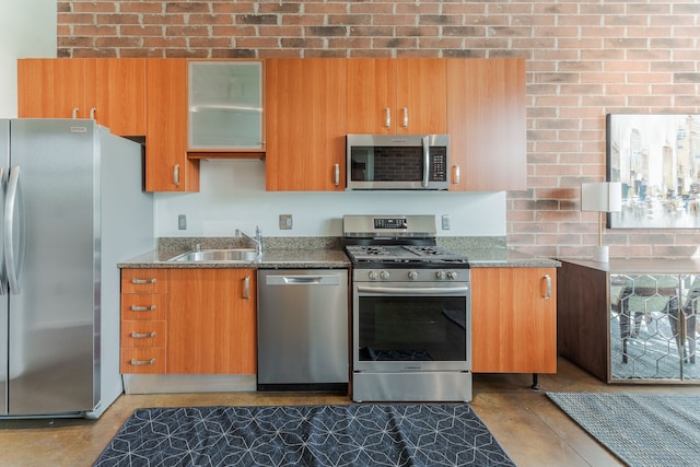 kitchen featuring a sink, brown cabinetry, light stone counters, glass insert cabinets, and appliances with stainless steel finishes