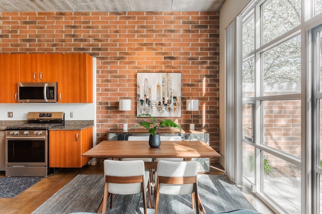 kitchen with brown cabinets, stainless steel appliances, brick wall, and dark stone countertops