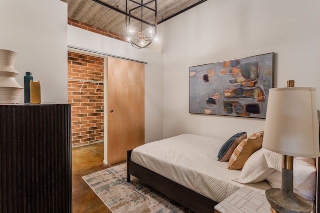bedroom featuring a notable chandelier, a closet, brick wall, and concrete flooring