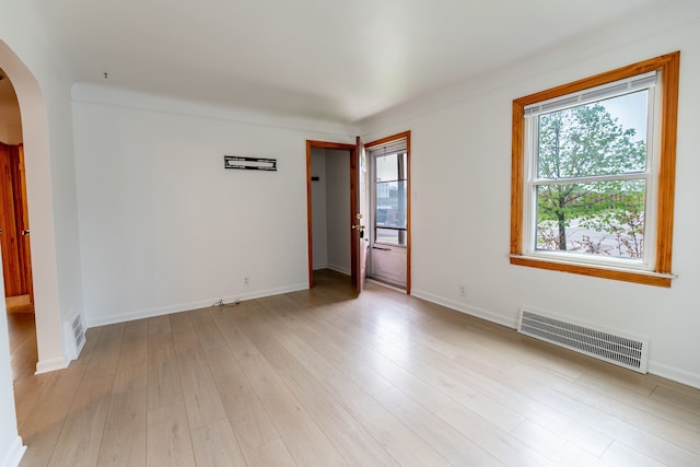 unfurnished room featuring light wood-type flooring, visible vents, baseboards, and arched walkways