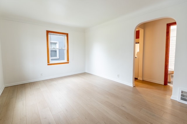 empty room with light wood-type flooring, visible vents, baseboards, and arched walkways