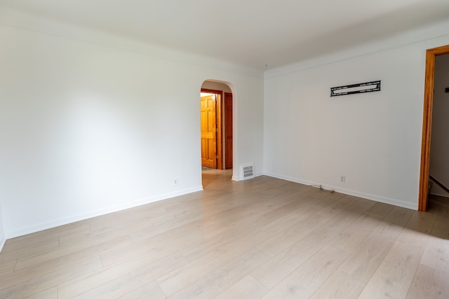 empty room with light wood-style flooring, arched walkways, baseboards, and visible vents