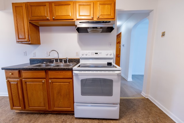 kitchen with under cabinet range hood, brown cabinetry, a sink, white range with electric cooktop, and dark countertops