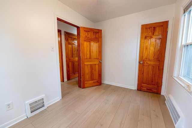 empty room featuring light wood-type flooring, visible vents, and baseboards