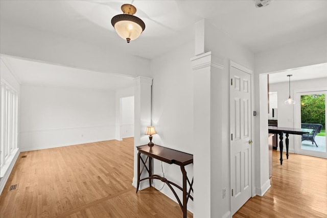 hallway featuring light wood-type flooring, baseboards, and decorative columns