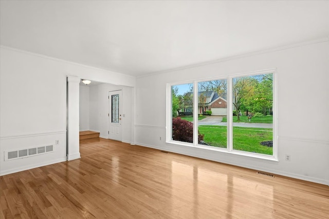 spare room featuring wood finished floors, crown molding, and baseboards
