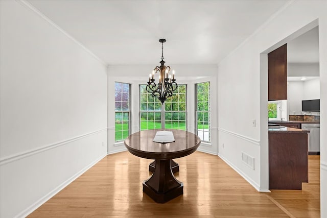 dining space with a chandelier, light wood-style floors, ornamental molding, and baseboards