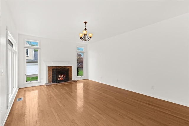 unfurnished living room with light wood-style floors, a chandelier, a brick fireplace, and healthy amount of natural light