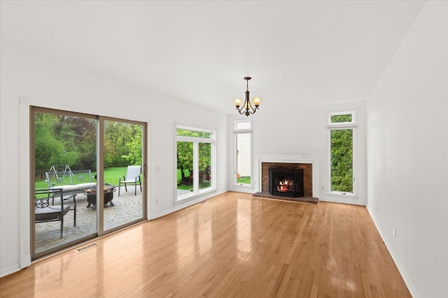 unfurnished living room featuring light wood finished floors, a chandelier, baseboards, and a brick fireplace