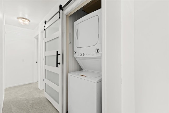 laundry room featuring stacked washing machine and dryer, a barn door, and light colored carpet