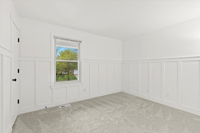 empty room featuring a decorative wall, light carpet, and a wainscoted wall