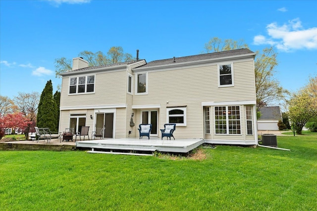 back of property with a wooden deck, a chimney, a lawn, central AC unit, and a fire pit